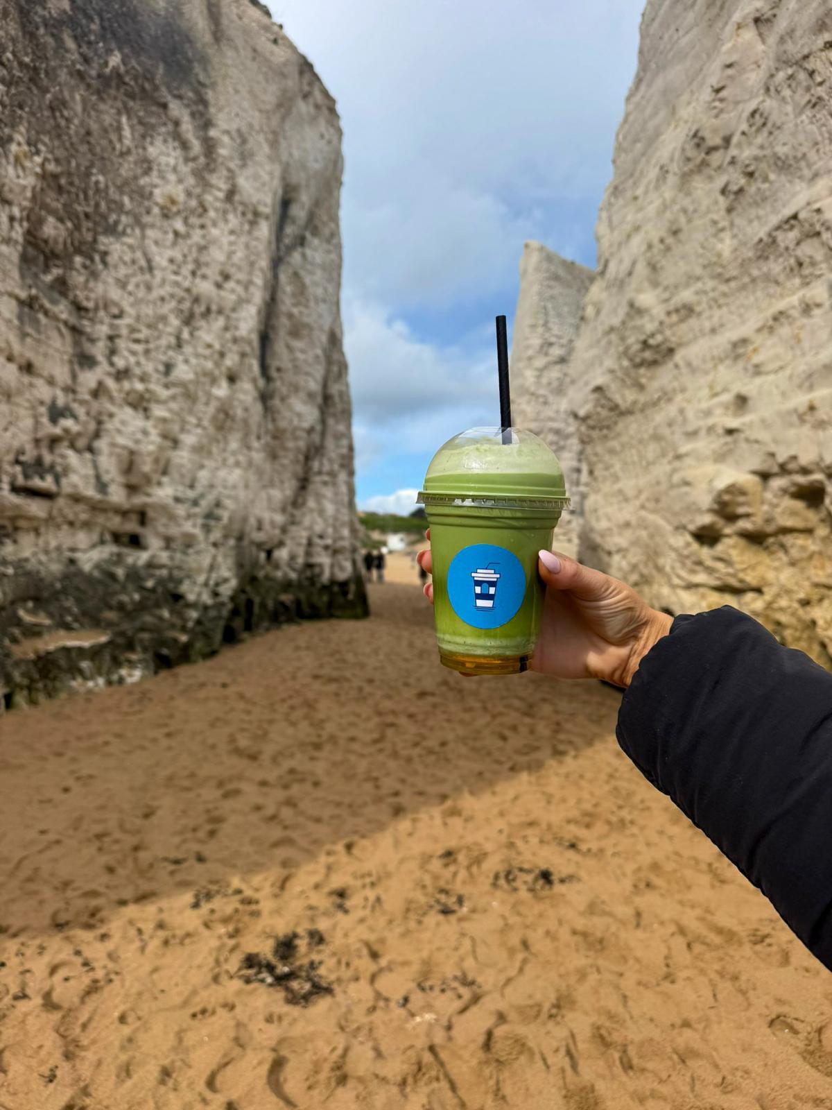 Brew & Bays matcha drink held between the cliffs at Botany Bay